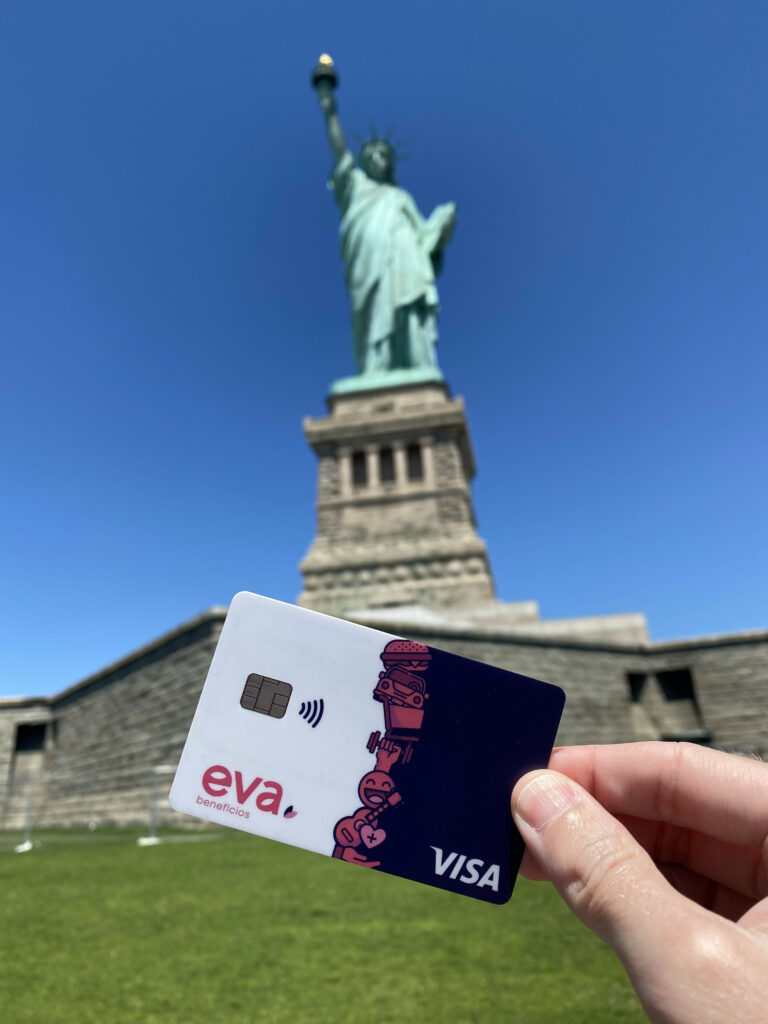 Uma mão segurando o cartão da Eva Benefícios com a Estátua da Liberdade ao fundo