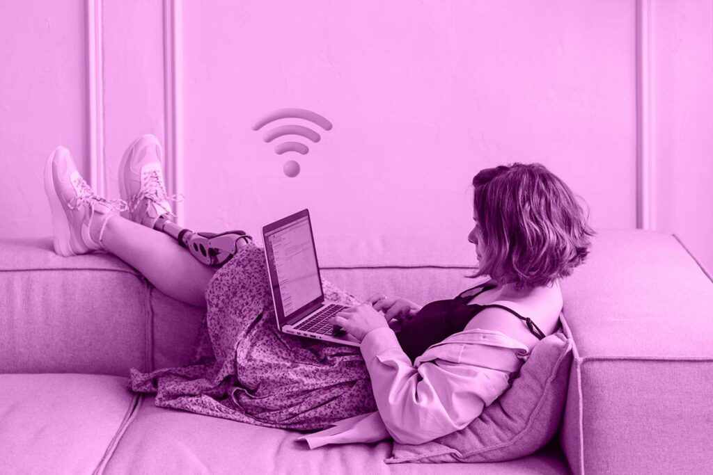 Mulher deitada no sofá digitando em um notebook. Acima do notebook está o ícone do wi-fi.
