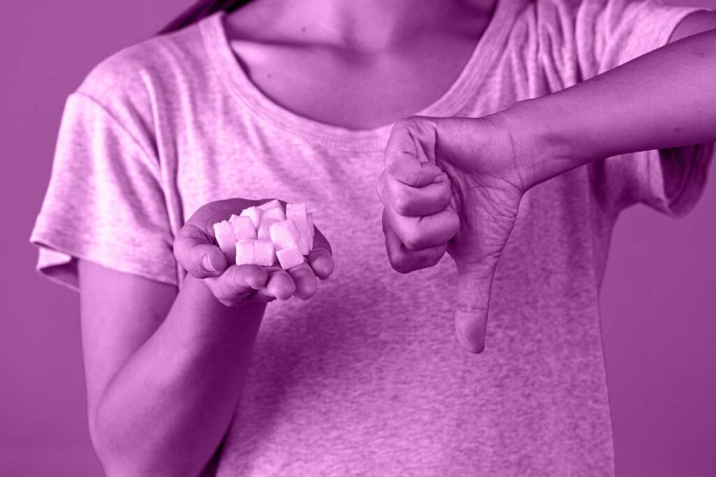 Mulher de camiseta branca segurando cubos de açúcar em uma mão enquanto, na outra, ela faz um sinal de reprovação.