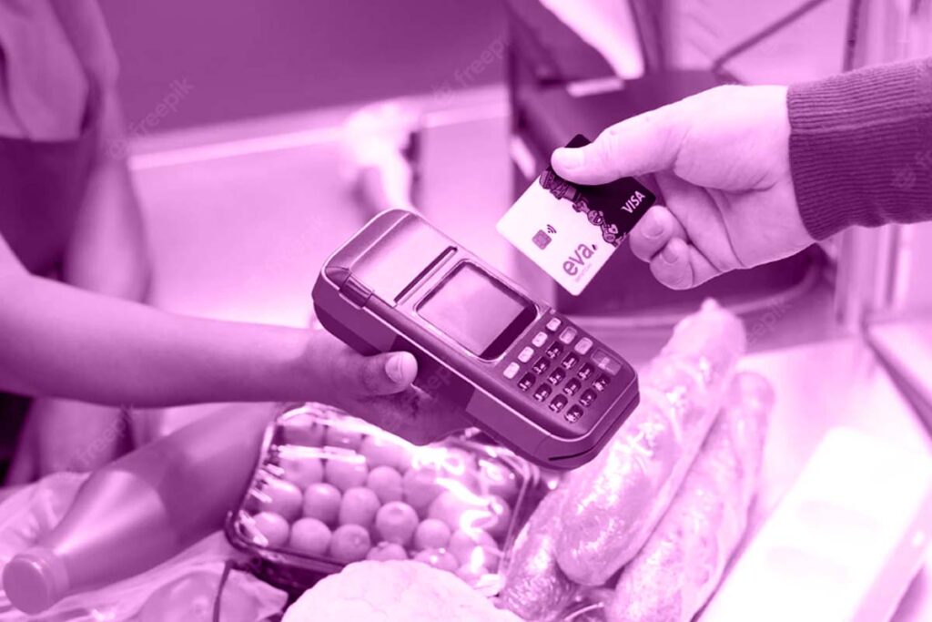 A imagem mostra as mãos de duas pessoas: uma caixa de supermercados segurando uma máquina de cartões e um cliente aproximando o cartão Eva da máquina.