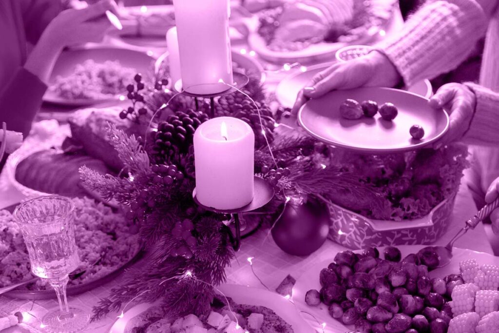 Mesa de ceia de natal com velas, frutas e pratos espalhadas sobre ela.