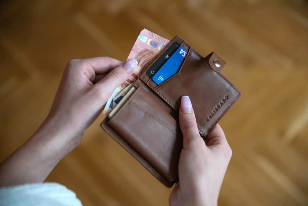 Um close de uma mão segurando uma carteira de couro marrom com cartões e notas de dinheiro, ideal para falar sobre finanças e organização.