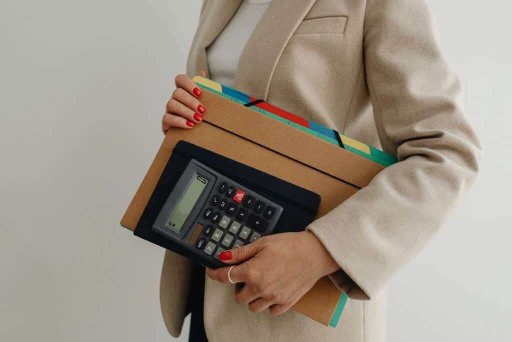 Mulher segurando uma calculadora e pastas organizadas, representando a importância da organização no trabalho e o uso de ferramentas adequadas para produtividade.