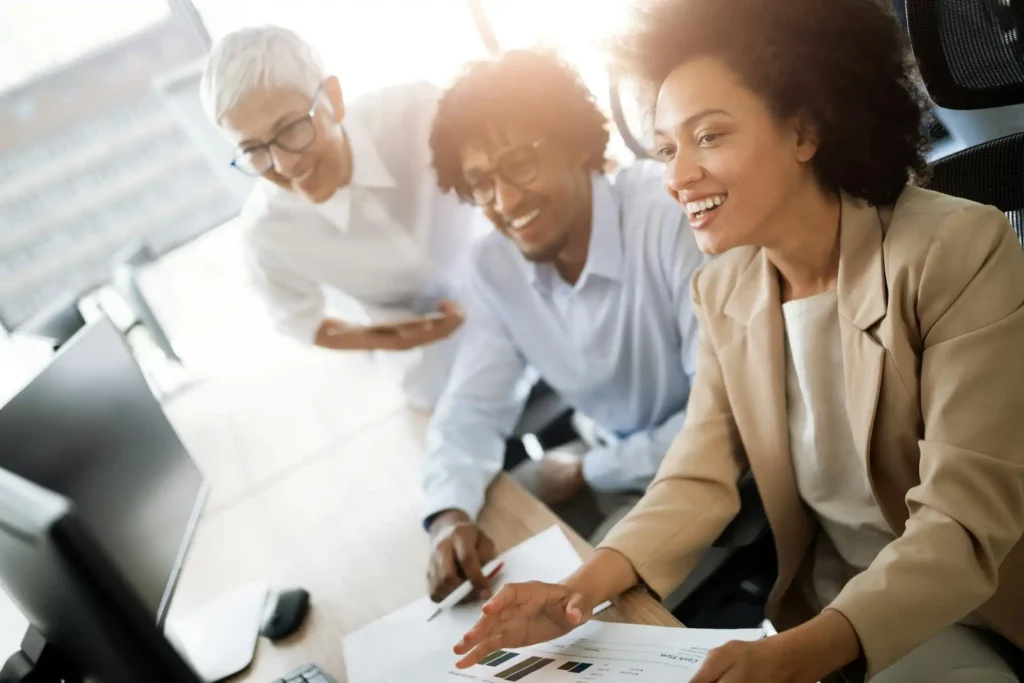 Grupo diverso de profissionais se reunindo em ambientes de trabalho modernos, discutindo dados e estratégias em frente a um computador.