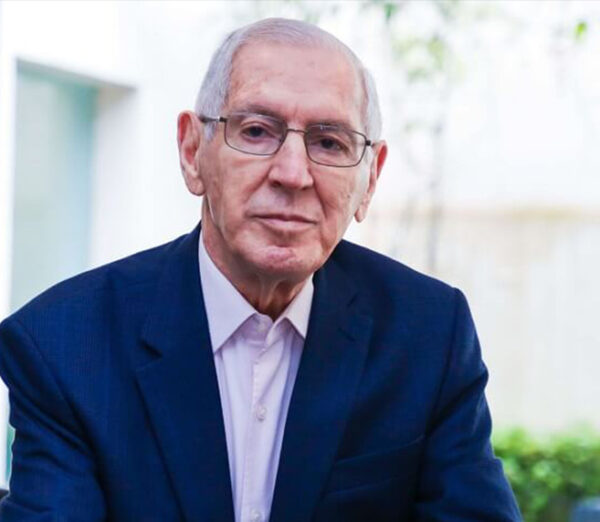 Foto de Idalberto Chiavenato, um homem branco, de cabelos brancos, calvo e com óculos. Além disso, ele está usando uma camisa branca por baixo de um paletó azul.