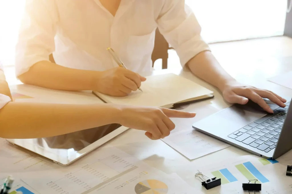 Duas pessoas discutindo sobre um projeto em um ambiente de escritório moderno, com documentos e um laptop sobre a mesa, evidenciando a colaboração e produtividade. | downsizing