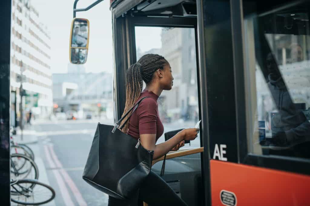 Mulher entrando no ônibus com uma bolsa, aguardando o transporte público em um ambiente urbano movimentado. Acessando o sistema de transporte de forma prática.