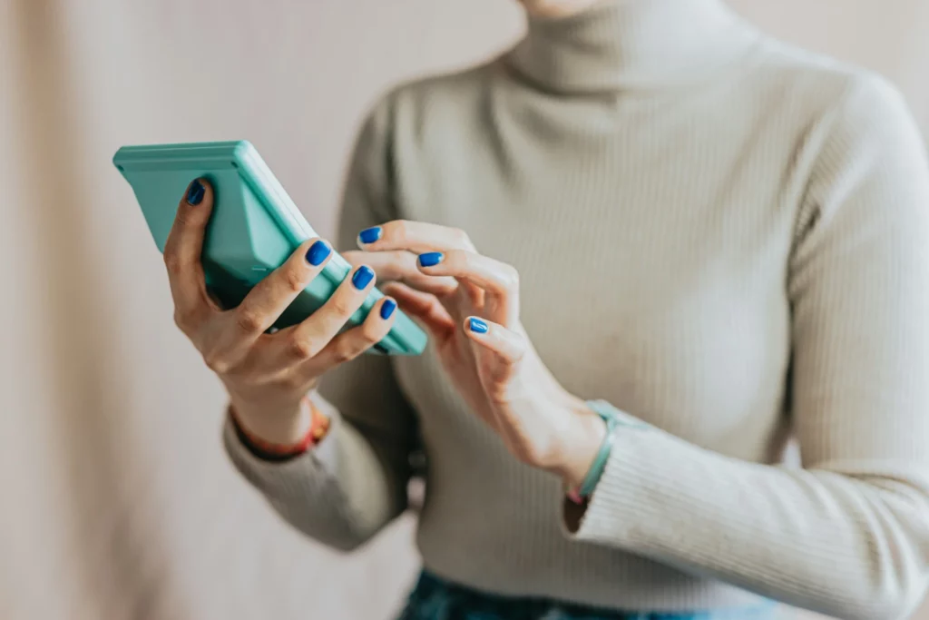 Mulher usando um smartphone azul enquanto digita. A cena é moderna e representa a tecnologia no cotidiano. | Reembolso de Despesas