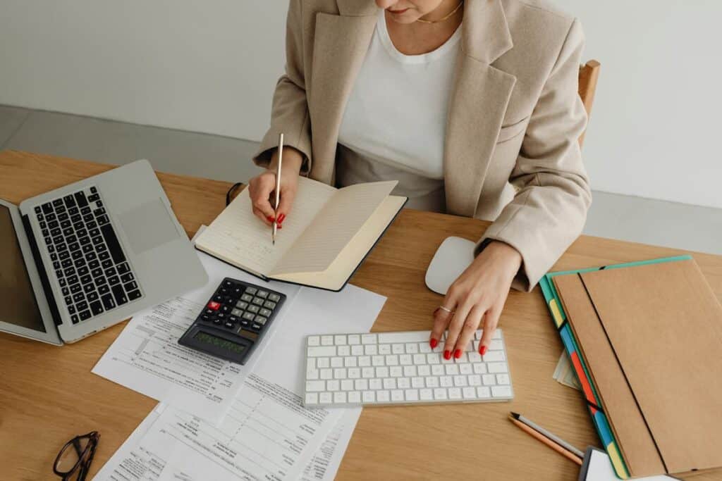 Pessoa analisando documentos financeiros com laptop e calculadora em mesa de escritório, representando a prestação de contas empresarial.