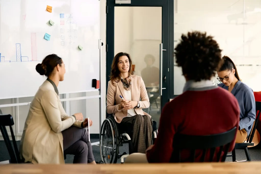 Reunião inclusiva em ambiente de trabalho moderno, com uma mulher em cadeira de rodas participando ativamente da discussão - Assiduidade no trabalho
