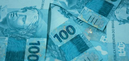Cédulas de 100 reais espalhadas sobre uma superfície, destacando o detalhe e a cor azul das notas utilizadas no Brasil.