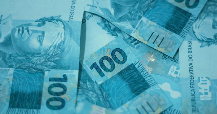 Cédulas de 100 reais espalhadas sobre uma superfície, destacando o detalhe e a cor azul das notas utilizadas no Brasil.