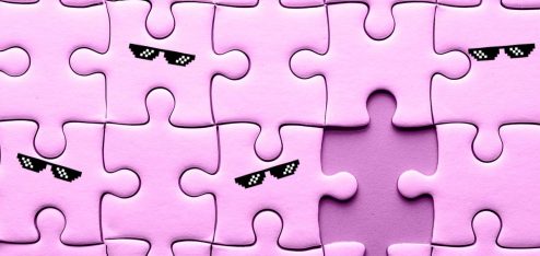 Peças de quebra cabeça de cor rosa e, entre elas, há uma faltando. Algumas das peças têm óculos escuros.
