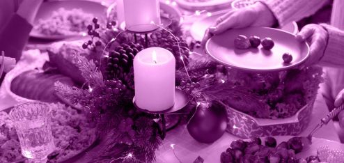 Mesa de ceia de natal com velas, frutas e pratos espalhadas sobre ela.