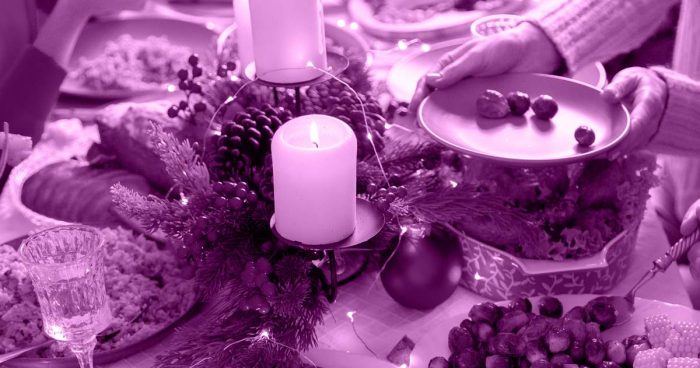 Mesa de ceia de natal com velas, frutas e pratos espalhadas sobre ela.