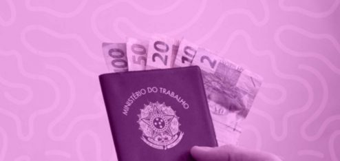 Na imagem há uma carteira de trabalho (CTPS), direito garantido pela CLT, com algumas notas de dinheiro dentro.