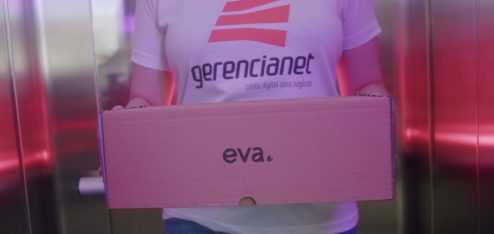 Mulher com camisa da Gerencianet saindo de um elevador carregando uma caixa escrito "Eva".