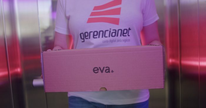 Mulher com camisa da Gerencianet saindo de um elevador carregando uma caixa escrito "Eva".