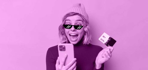 Mulher de touca e óculos escuros segurando o celular em uma mão e o Evacard em outra, com uma expressão de surpresa.