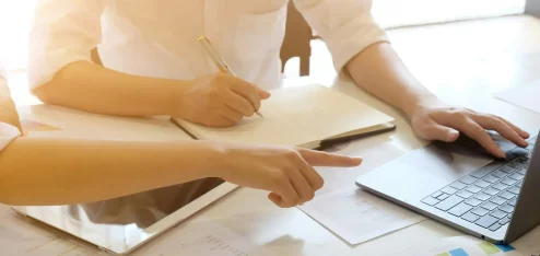 Duas pessoas discutindo sobre um projeto em um ambiente de escritório moderno, com documentos e um laptop sobre a mesa, evidenciando a colaboração e produtividade. | downsizing
