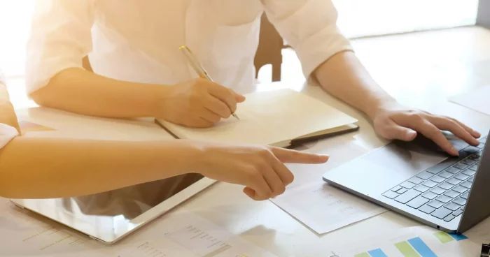 Duas pessoas discutindo sobre um projeto em um ambiente de escritório moderno, com documentos e um laptop sobre a mesa, evidenciando a colaboração e produtividade. | downsizing