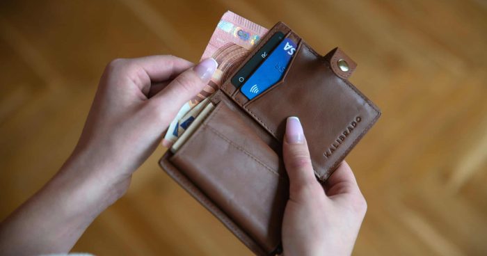 Um close de uma mão segurando uma carteira de couro marrom com cartões e notas de dinheiro, ideal para falar sobre finanças e organização.