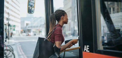 Mulher entrando no ônibus com uma bolsa, aguardando o transporte público em um ambiente urbano movimentado. Acessando o sistema de transporte de forma prática.