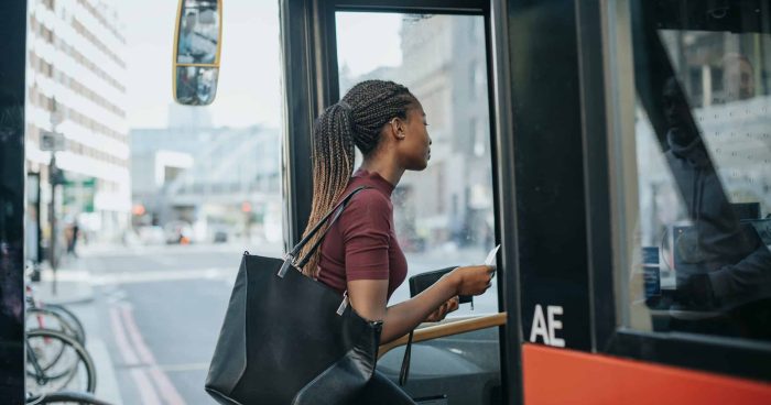 Mulher entrando no ônibus com uma bolsa, aguardando o transporte público em um ambiente urbano movimentado. Acessando o sistema de transporte de forma prática.
