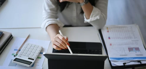 Mulher trabalhando em um tablet com calculadora e documentos, representando o ambiente de trabalho e produtividade em escritório.