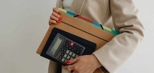 Mulher segurando uma calculadora e pastas organizadas, representando a importância da organização no trabalho e o uso de ferramentas adequadas para produtividade.