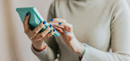 Mulher usando um smartphone azul enquanto digita. A cena é moderna e representa a tecnologia no cotidiano. | Reembolso de Despesas