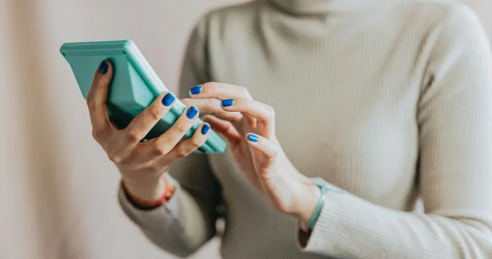 Mulher usando um smartphone azul enquanto digita. A cena é moderna e representa a tecnologia no cotidiano. | Reembolso de Despesas