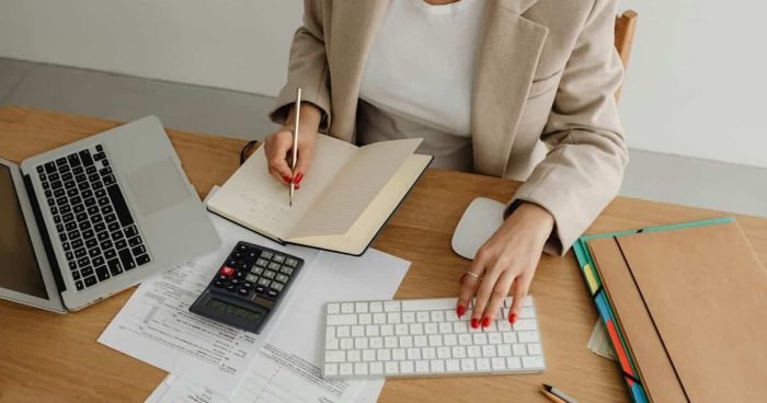 Pessoa analisando documentos financeiros com laptop e calculadora em mesa de escritório, representando a prestação de contas empresarial.