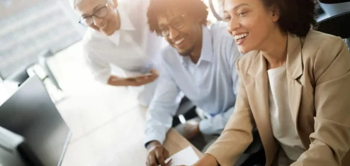 Grupo diverso de profissionais se reunindo em ambientes de trabalho modernos, discutindo dados e estratégias em frente a um computador.