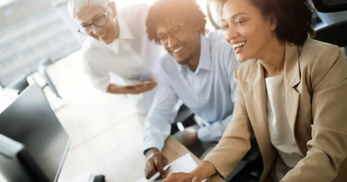 Grupo diverso de profissionais se reunindo em ambientes de trabalho modernos, discutindo dados e estratégias em frente a um computador.