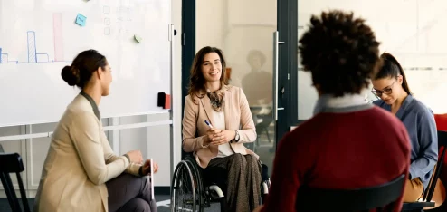Reunião inclusiva em ambiente de trabalho moderno, com uma mulher em cadeira de rodas participando ativamente da discussão - Assiduidade no trabalho