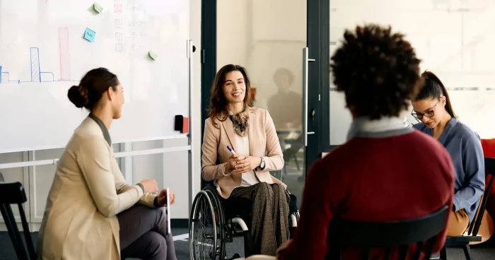 Reunião inclusiva em ambiente de trabalho moderno, com uma mulher em cadeira de rodas participando ativamente da discussão - Assiduidade no trabalho