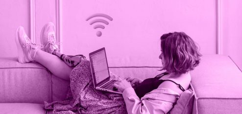 Mulher deitada no sofá digitando em um notebook. Acima do notebook está o ícone do wi-fi.